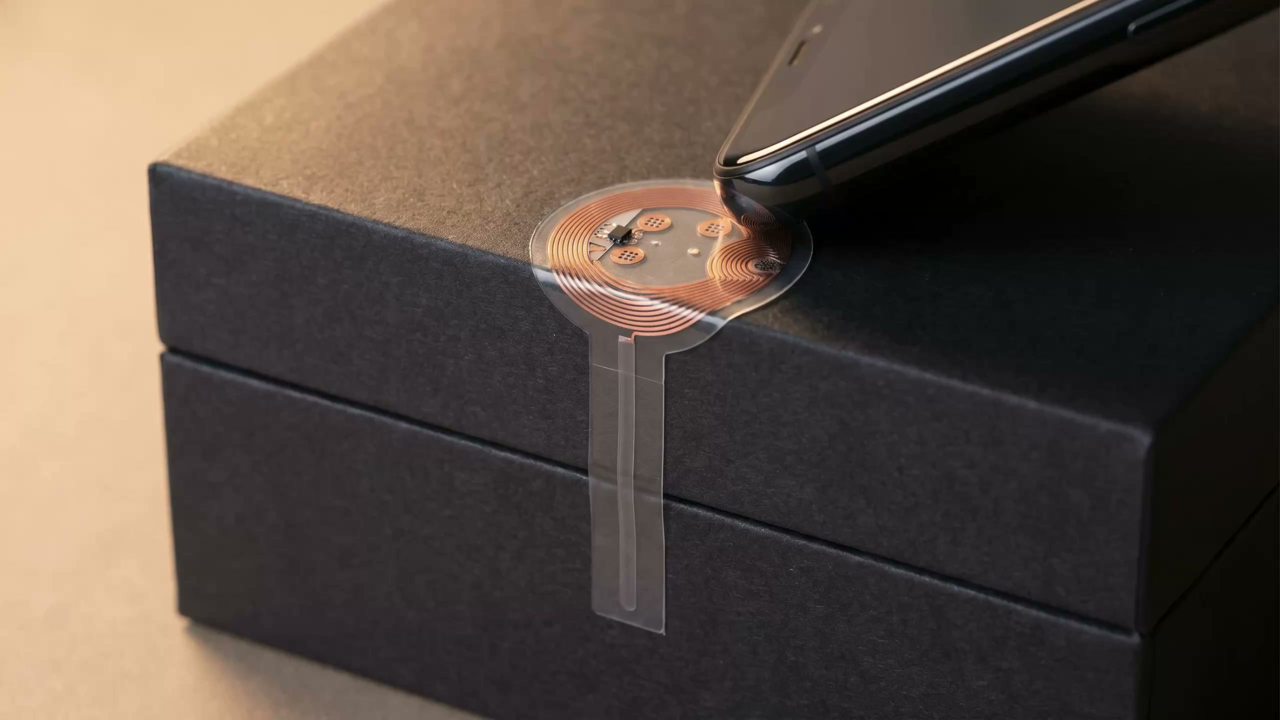Tag NFC tamper loop dont la languette de détection barre le joint du couvercle d'une boîte, scanné par un téléphone